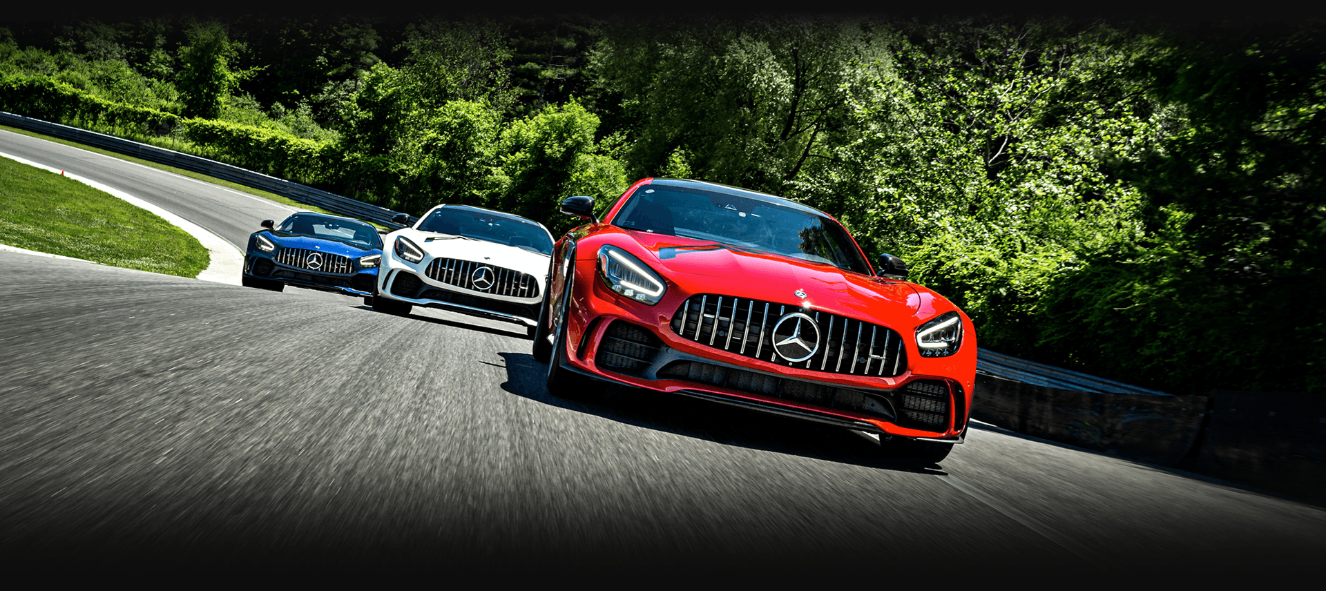 4)	Three Mercedes-AMG vehicles, red, white and blue racing on Lime Rock Park track