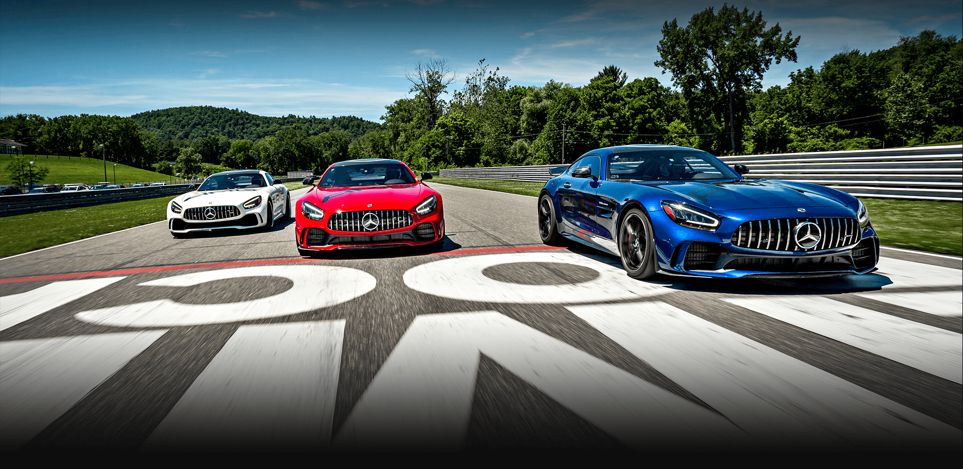 Three Mercedes-AMG vehicles, red, white and blue racing on Lime Rock Park track