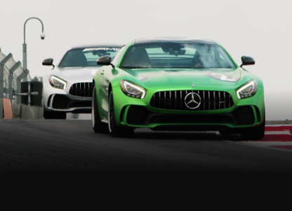White and green Mercedes-AMG vehicles racing on track.